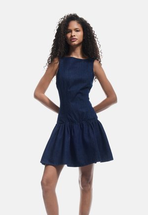 Donkerblauwe denimjurk met een getailleerde bovenkant, brede halslijn en een uitlopende, ruches rok. Soepele textuur met minimale stiksels.