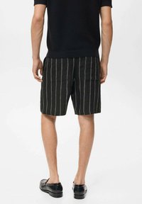 Pantaloni scurți negri cu dungi verticale albe, dintr-un material texturat. Prezintă două buzunare la spate, purtați împreună cu un top negru din tricot și încălțăminte neagră.