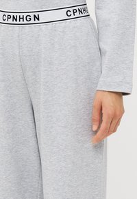 Grå joggebukser med hvit livvidde som har svart tekst "CPNHGN." Stoffet ser mykt ut med en jevn tekstur, og viser et enkelt design.