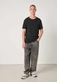 Črna majica s kratkimi rokavi, sive široke kavbojke z brezhibnim pranjem in sive superge z belimi poudarki. Obleka ima sproščen kroj in priložnostni slog.