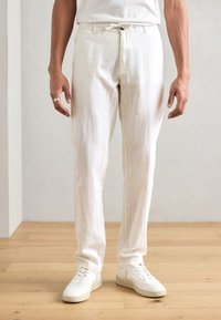 Vita linnebyxor med avslappnad passform, utrustade med elastisk dragsko i midjan och subtil textur, matchade med vita sneakers.