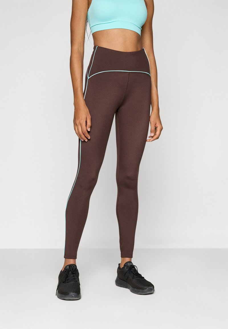 Brune høyt liv leggings med lyseblå sidesømmer, laget av et glatt, elastisk stoff. Kombinert med en lyseblå crop top og svarte joggesko.