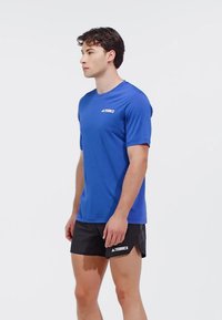 Camiseta atlética de manga corta azul con logo en el pecho, combinada con pantalones cortos negros. Textura suave, diseño ajustado y dobladillo hasta la rodilla.