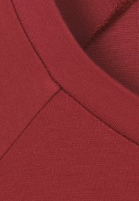 Débardeur rouge cintré avec une finition lisse et texturée. Présente un col rond et des coutures le long des épaules.