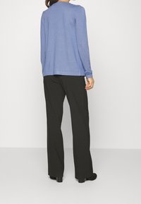 Haut bleu clair à manches longues avec un col arrondi, porté avec un pantalon noir. Matière douce (mélange de coton) et coupe décontractée, sans motifs ni accents.