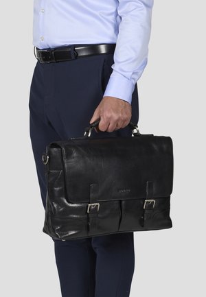 Black leather briefcase with silver hardware, top handle, two front buckles, smooth texture, and a spacious interior, held by a person.