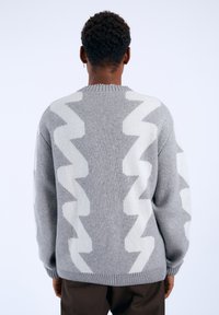 Gray knit sweater featuring a zigzag pattern in white, ribbed collar and cuffs, with a relaxed fit and soft texture.
