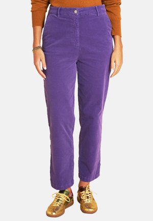 Lila Cordhosen in geradem Schnitt, mit einem Knopfverschluss vorne und Seitentaschen, kombiniert mit goldenen und mehrfarbigen Sneakers.