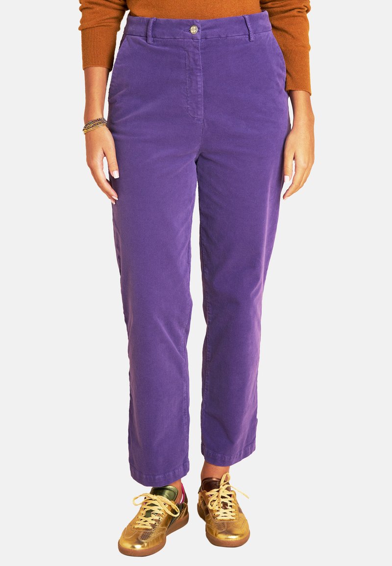 Lila Cordhosen in geradem Schnitt, mit einem Knopfverschluss vorne und Seitentaschen, kombiniert mit goldenen und mehrfarbigen Sneakers.