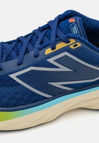 Baskets de course bleues avec une tige en mesh, des accents argentés et une semelle rembourrée avec des détails bleus et verts. Marque notable sur la languette.