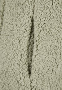 Zachte, lichtgrijze sherpa fleece stof met een dichte, krullende textuur en een verticale naad die in het midden loopt.