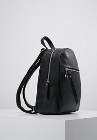 Czarny skórzany plecak o zaokrąglonym kształcie, z dwoma zamykanymi na zamek przegrodami i regulowanymi paskami na ramiona; gładka faktura i minimalistyczny design.