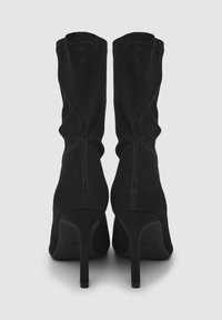 Czarne kozaki do kolan na obcasie o gładkiej, zamszowej fakturze, dopasowanym kroju i wyraźnych przeszyciach wzdłuż tylnego szwu.