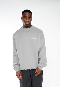 Felpa grigia con colletto rotondo, vestibilità oversized e logo ricamato "MULTIPLY" in bianco sul lato sinistro. Tessuto morbido.