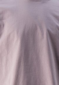 Camiseta de color lila claro hecha de suave algodón, con un escote redondo y textura lisa, con sutiles arrugas visibles en la tela.