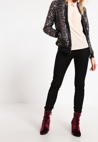 Veste bomber en imprimé léopard avec des accents noirs, pantalon noir ajusté et bottines en velours bordeaux. Tissu doux, poignets et taille côtelés.
