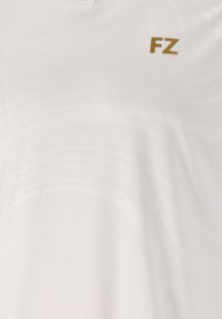 Valkoinen polo-paita, jossa on hienovarainen aalto-kuvio, FZ-logo kullanvärisenä. Valmistettu sileästä, kevyestä kankaasta mukavuutta ja hengittävyyttä varten.
