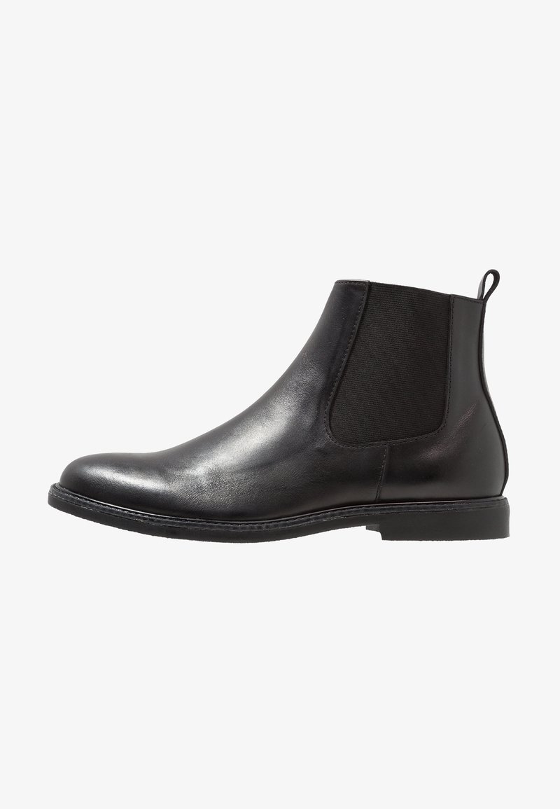 Bottine Chelsea en cuir noir avec des panneaux élastiques sur les côtés et une boucle à l'arrière, dotée d'une semelle basse et plate, et d'une finition lisse et brillante.