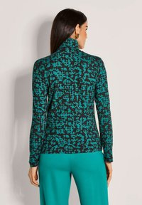 Langärmliger Rollkragenpullover in Schwarz mit einem türkisfarbenen abstrakten Muster. Weicher, dehnbarem Stoff. Kombiniert mit passenden türkisfarbenen Hosen.