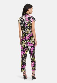 Blommig jumpsuit med korta ärmar och krage. Har svart bakgrund med rosa, grön och vit tryck. Figursydd silhuett med smalnade byxor.