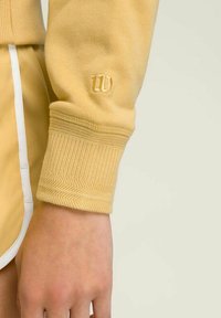 Pullover giallo con polsini a costina, caratterizzato da un motivo testurizzato, logo ricamato sulla manica e finitura in tessuto liscia.