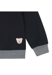 Schwarzer Baumwoll-Sweatshirt mit strukturiertem Material, gestreiften Rippbündchen und einem gestickten Bärenkopf auf der Brust.