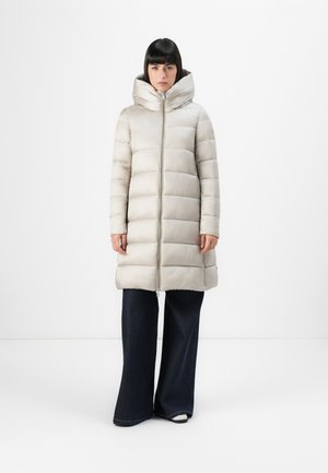 Lichtbeige pufferjas met een hoge kraag, ritsluiting en gestikte paneelontwerp. Draagt over donkere, wijde jeans. Zachte, gladde textuur.