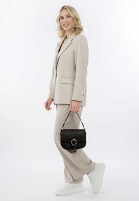 Beige op maat gemaakt pak met flare-broeken, gecombineerd met een kleine zwarte leren handtas met een ronde hardwareaccent. Witte sneakers.