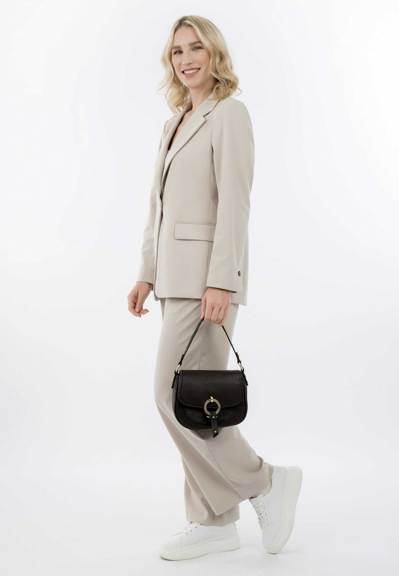 Beige op maat gemaakt pak met flare-broeken, gecombineerd met een kleine zwarte leren handtas met een ronde hardwareaccent. Witte sneakers.