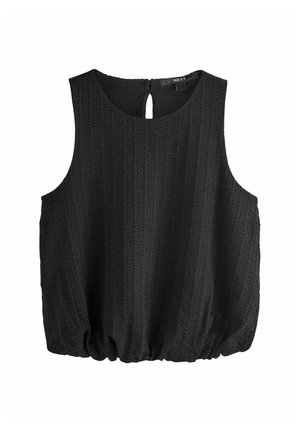 Kobieta w czarnej bluzce na ramiączkach, ciemnej mini spódnicy dżinsowej z przednim zamkiem błyskawicznym oraz kolorowych klapkach z klamrą, stojąca na jednolitym tle.