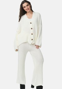 Gilet oversize en tricot de couleur crème avec cinq grands boutons, associé à un pantalon large à côtes, offrant une coupe décontractée et une texture douce.