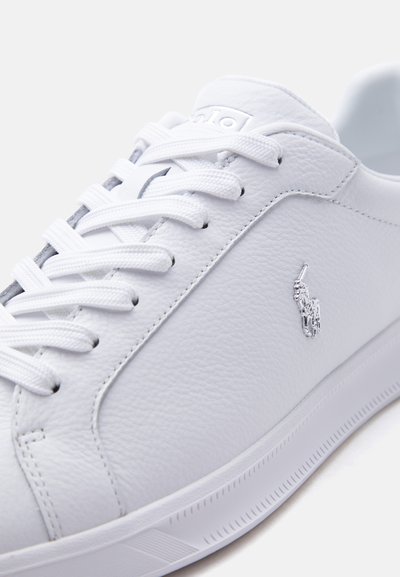 Λευκό δερμάτινο αθλητικό παπούτσι με λευκά κορδόνια, υφή στην επιφάνεια και μεταλλικό λογότυπο Polo Ralph Lauren στο πλάι.