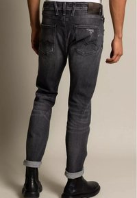 Slim-fit tmavě šedé džíny z džínoviny, s jemným opotřebením, ohrnutými nohavicemi a dvěma zadními kapsami se zigzagovým stehem.