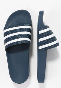 Mörkblåa slidesandaler med vit tre-stripesdesign, texturerad ovandel och platt sula. Tillverkade av syntetiskt material med en slät yta.