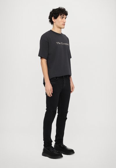 Camiseta negra de gran tamaño con un logo sutil, combinada con jeans ajustados negros rasgados y zapatos chunky negros. Tejido suave y corte relajado.