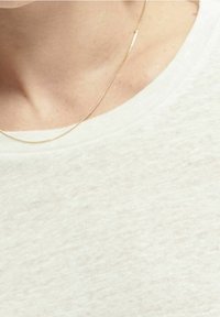 Primo piano di un collo umano con indosso una sottile collana d'oro e una camicia beige chiaro texturizzata.