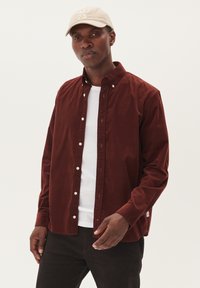 Corduroy overhemd in donkerbordeaux met een button-down kraag, voorzien van witte knopen en een gebogen zoom, gelaagd over een wit T-shirt.