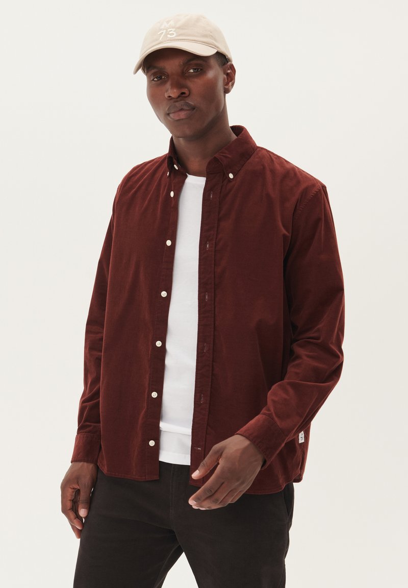 Corduroy overhemd in donkerbordeaux met een button-down kraag, voorzien van witte knopen en een gebogen zoom, gelaagd over een wit T-shirt.
