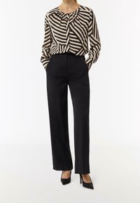 Pantaloni neri a vita alta abbinati a una camicetta a maniche lunghe con motivo a righe beige e nere e scollatura arricciata.