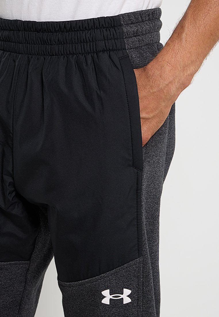 Pantalones deportivos grises con paneles laterales negros, presentan una cinturilla elástica y una textura suave, adornados con un logo blanco en la parte inferior de la pierna.