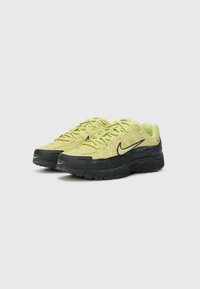 Ténis Nike amarelos e pretos com parte superior texturada, bico redondo e sola acolchoada. Apresenta um logótipo proeminente e atacadores em contraste.
