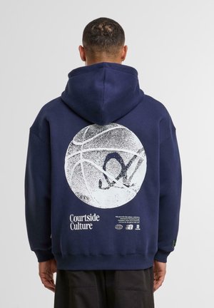 Hoodie bleu marine avec un graphique de basket-ball texturé en blanc à l'arrière, texte "Courtside Culture" et poignets côtes. Tissu doux, coupe décontractée.