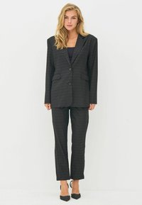 Black tailored suit made of textured fabric, featuring a single-breasted blazer with two pockets and matching straight-leg trousers.