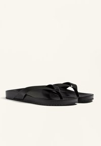Flip-flops negre din cauciuc, cu o textură netedă, talpă plată și bretele în cruce. Design simplu, fără modele sau detalii suplimentare.