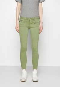 Green skinny jeans made of denim, featuring two front pockets with zippers, paired with a gray T-shirt and white high-top sneakers.