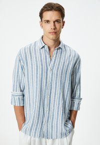 Camisa ligera de manga larga con botones, con rayas verticales en azul y blanco, un cuello casual y mangas enrolladas, hecha de tela suave.