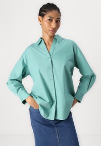 Una camicia azzurro chiaro con colletto e maniche lunghe, realizzata in tessuto morbido. Abbinata a una gonna di jeans per un look casual.