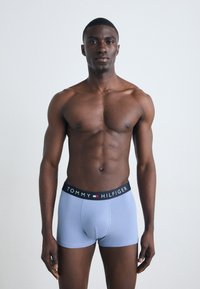 Kék pamut boxer alsónadrág fekete derékrésszel, amelyen a "TOMMY HILFIGER" logó fehér, piros és kék színekben található. Az alsónadrág szorosan illeszkedik és bordázott.