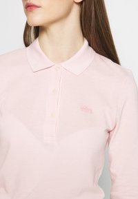 Polo shirt rosa chiaro realizzato in tessuto testurizzato, con colletto classico, patta con tre bottoni e un piccolo logo ricamato sul petto.