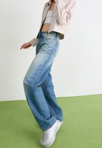 Light blue denim jeans with a relaxed fit, light wash fading, and straight legs. Paired with white platform shoes and a cropped beige jacket.